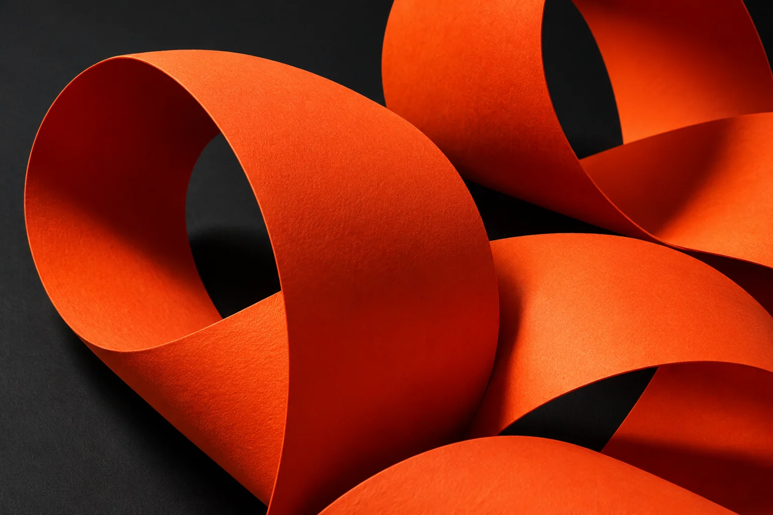 Escultura de papel naranja con curvas entrelazadas sobre un fondo negro